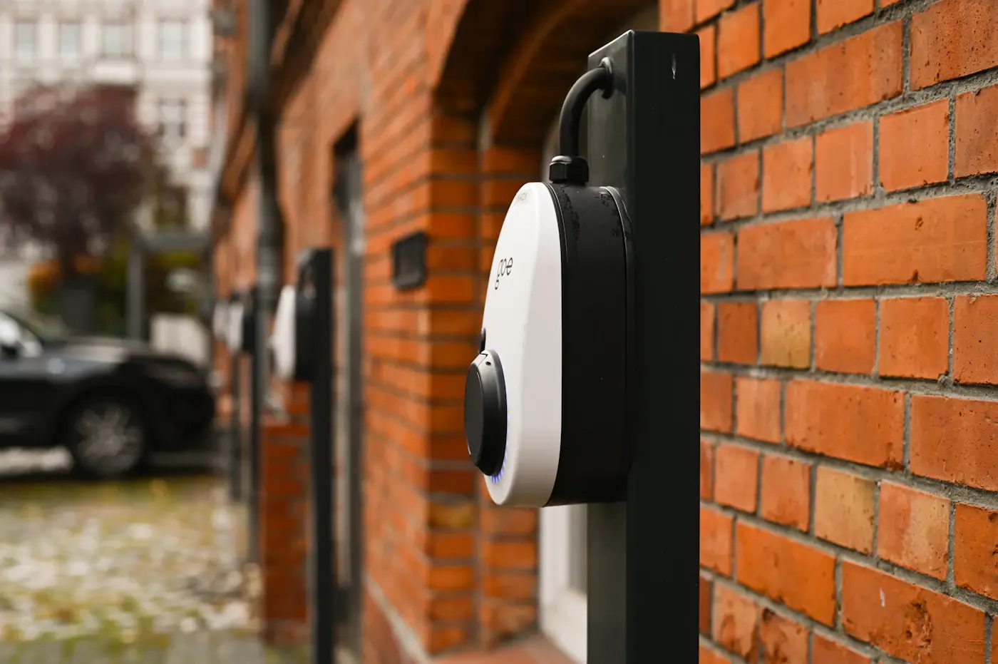 Plusieurs bornes de recharge alignées le long de la façade en brique d'un immeuble d'habitation.
