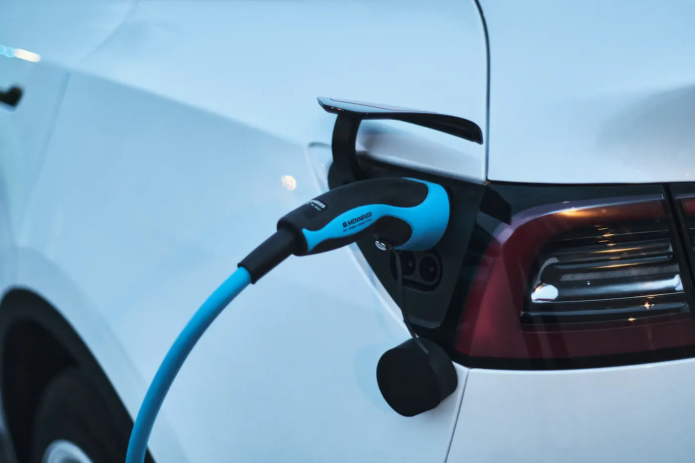 Gros plan sur un connecteur de recharge branché à la trappe d'une voiture électrique blanche.