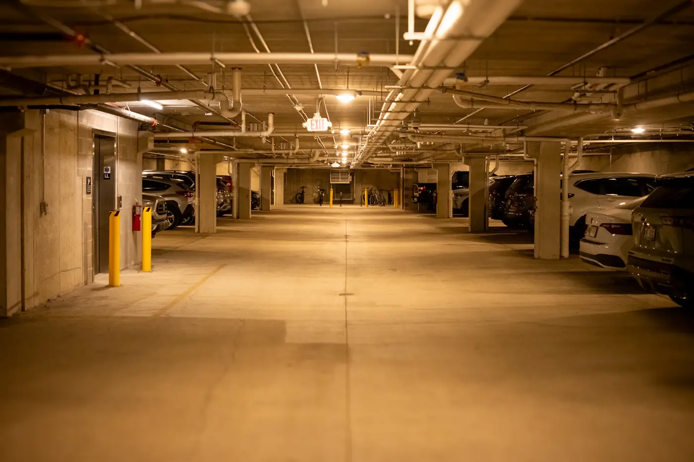 Un parking collectif en sous-sol, ses places numérotées et ses véhicules stationnés le long des piliers.
