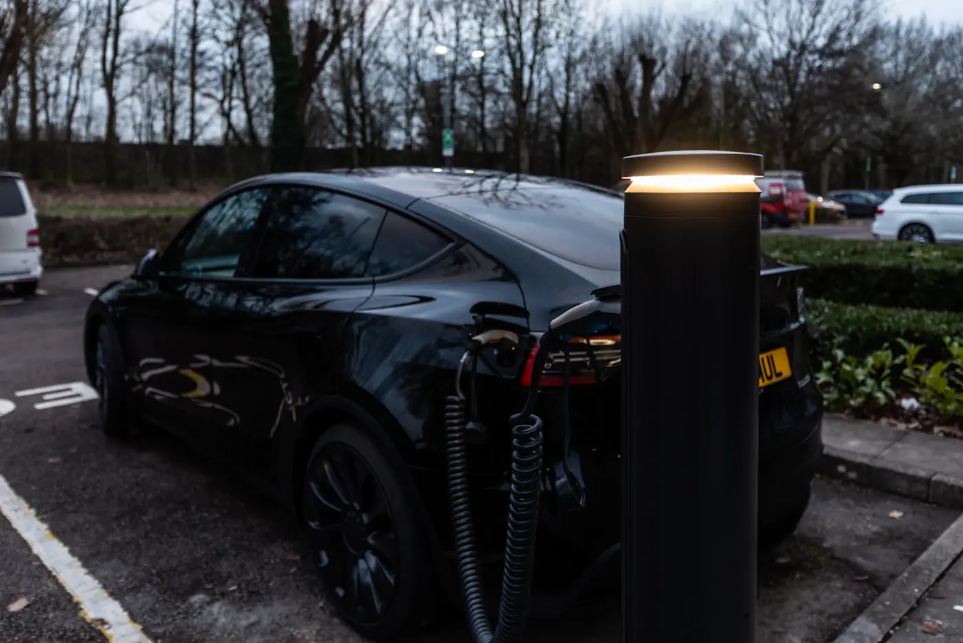 Une voiture électrique en charge sur une borne sur pied, au bord d'une place de stationnement.