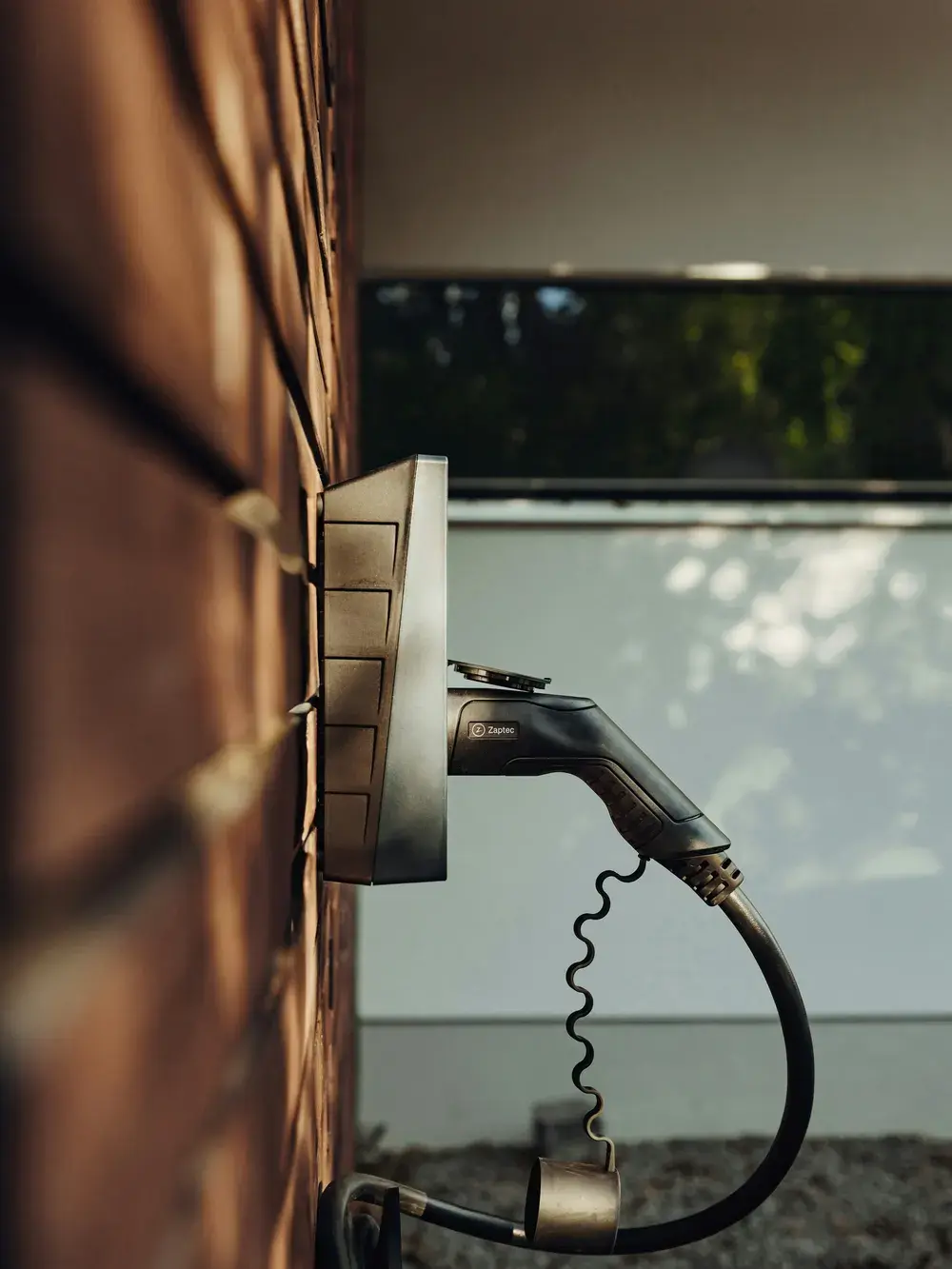 Une borne de recharge murale vue de profil, son connecteur au repos sur son support, contre un mur de brique.